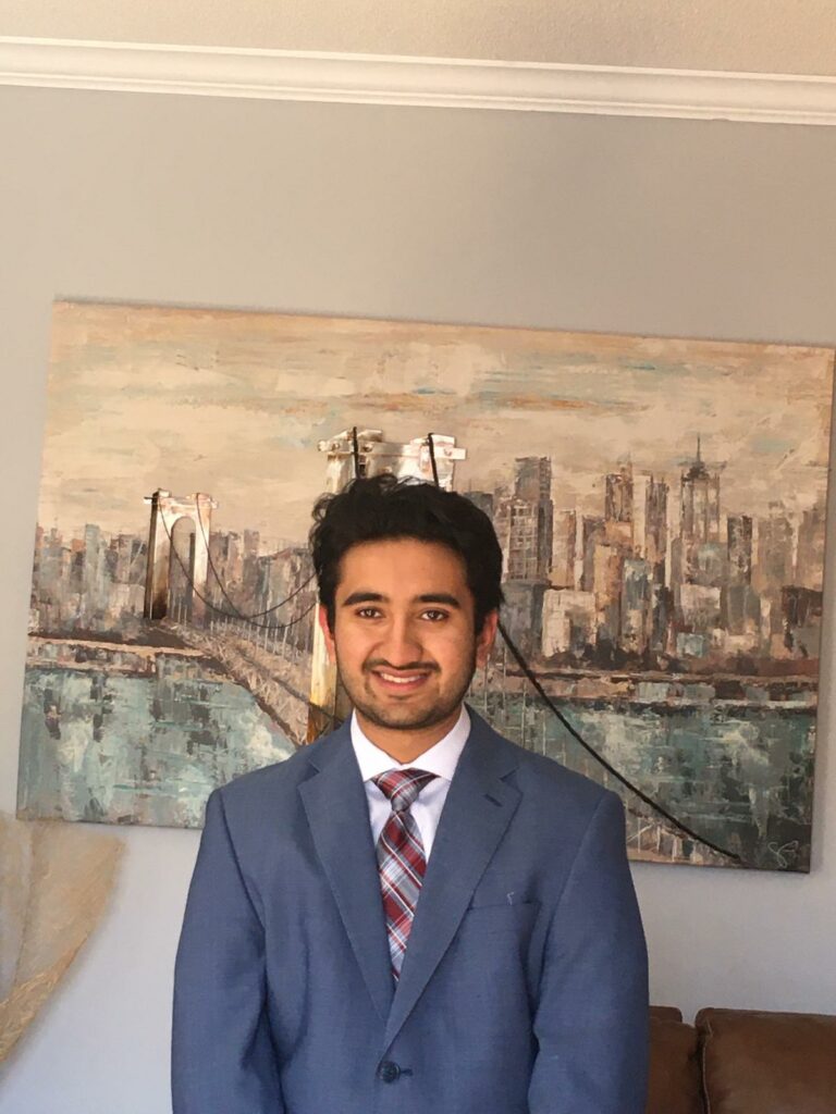 Pratah in a suit in front of a painting of a skyline